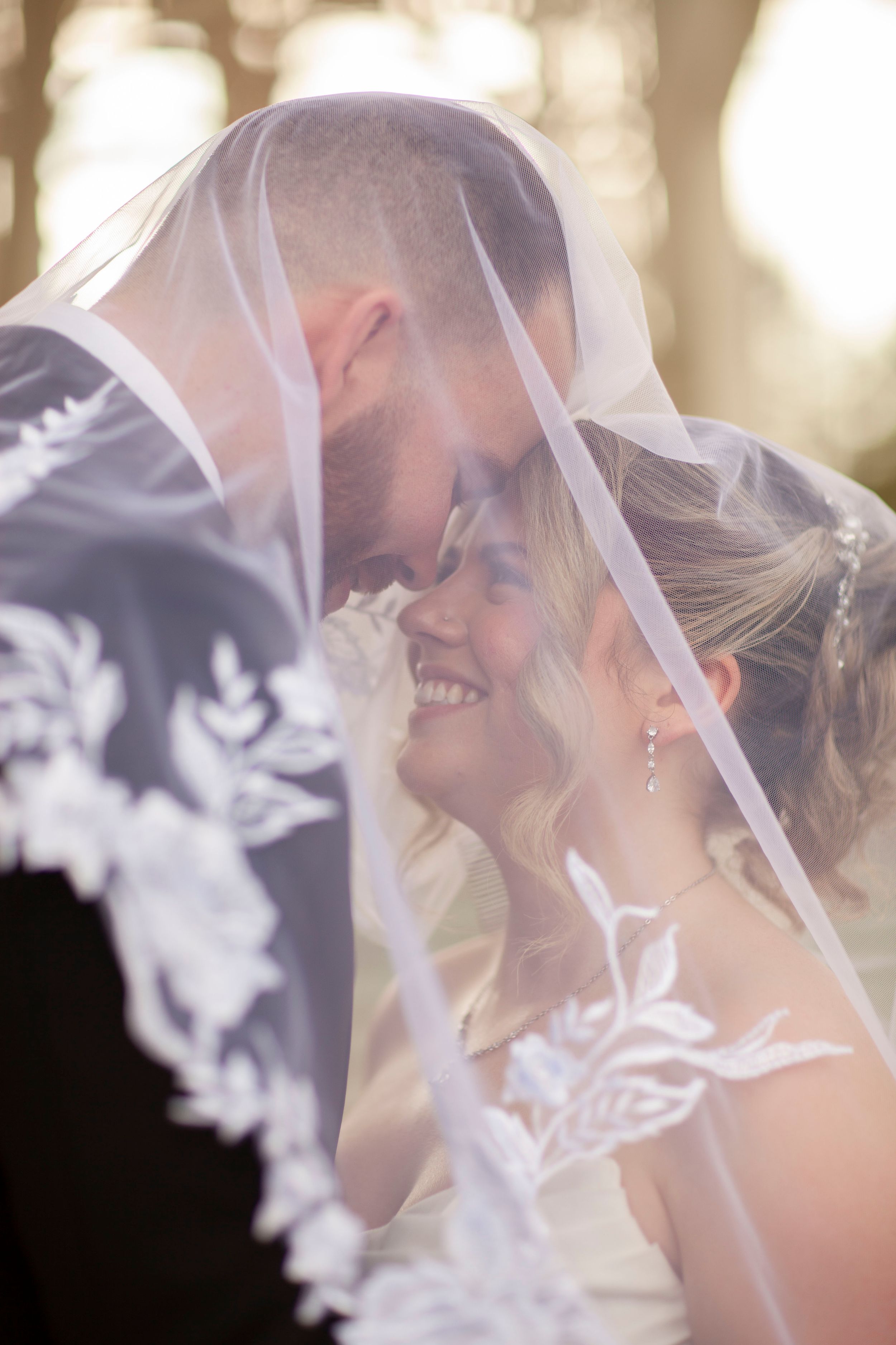 Romantic wedding portrait of bride and groom sharing an intimate moment under a lace veil.