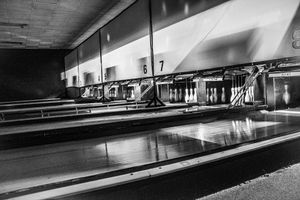 Black and white photo of empty bowling alley lanes with pins set at the end under numbered lane markers.