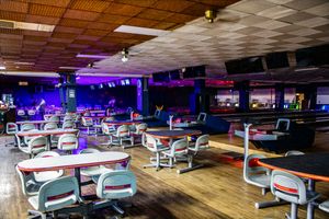 Empty bowling alley with colorful neon lights, rows of tables and chairs, and multiple lanes in the background.