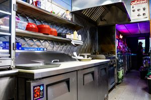 Stainless steel commercial kitchen interior with shelving, red bowls, and industrial equipment under purple lighting.