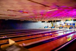 Colorful bowling alley lanes illuminated by vibrant pink and purple neon lights in a retro bowling center.