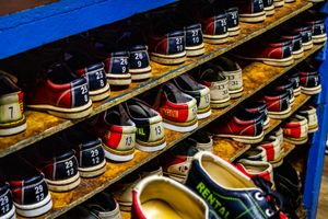 Rows of colorful rental bowling shoes with size numbers displayed on wooden shelves at a bowling alley.