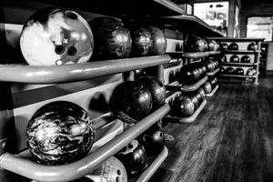 Black and white photo of bowling balls arranged on metal racks in a bowling alley.