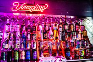 A colorful bar display featuring Yuengling neon sign above rows of liquor bottles lit with purple and pink lighting.
