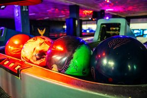 Colorful bowling balls resting in a ball return rack at a vibrant bowling alley with neon lights.