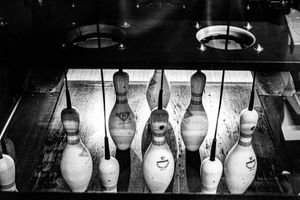 Close-up black and white photo of bowling pins arranged on a rack at the end of a bowling lane.