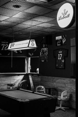 Black and white photo of a bar with a pool table, Miller Lite lamp, Labatt sign, and Buffalo Bills jersey #17 Allen.