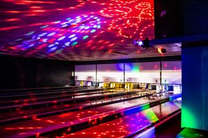 Colorful disco lights illuminate a bowling alley with neon red, blue, and green reflections on lanes during cosmic bowling night.