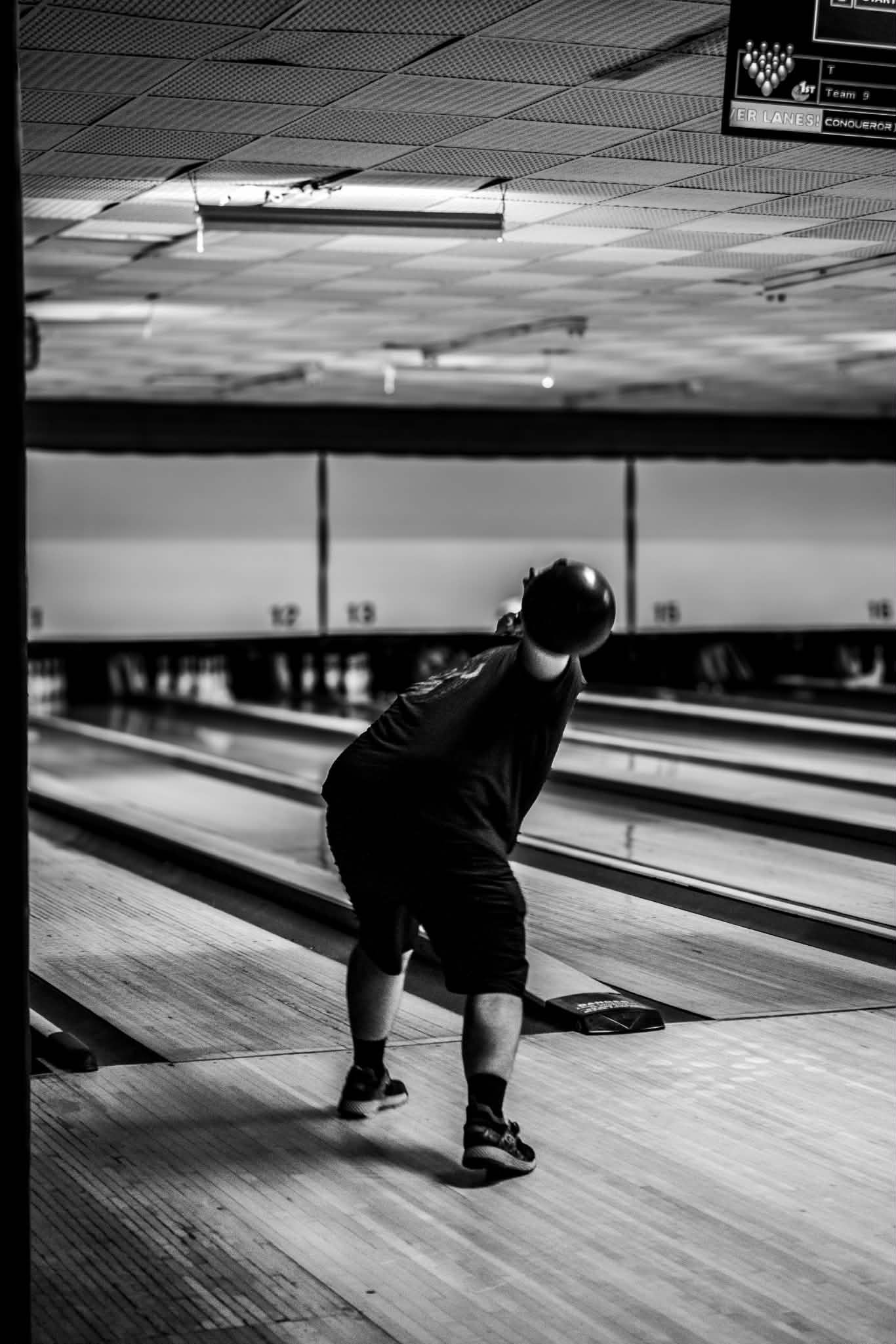 Black and white photo of a bowler releasing a ball down a bowling alley lane.