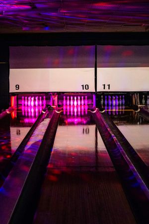 Bowling alley lanes 9, 10, and 11 illuminated with vibrant pink and purple neon lights reflecting off the wooden floors.