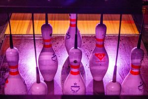 Bowling pins illuminated by purple neon lights on a glossy lane, creating a vibrant glow effect.