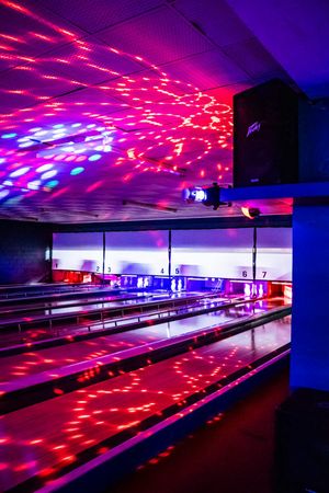 Bowling alley with vibrant pink and purple disco lights illuminating the lanes during a cosmic bowling night event.