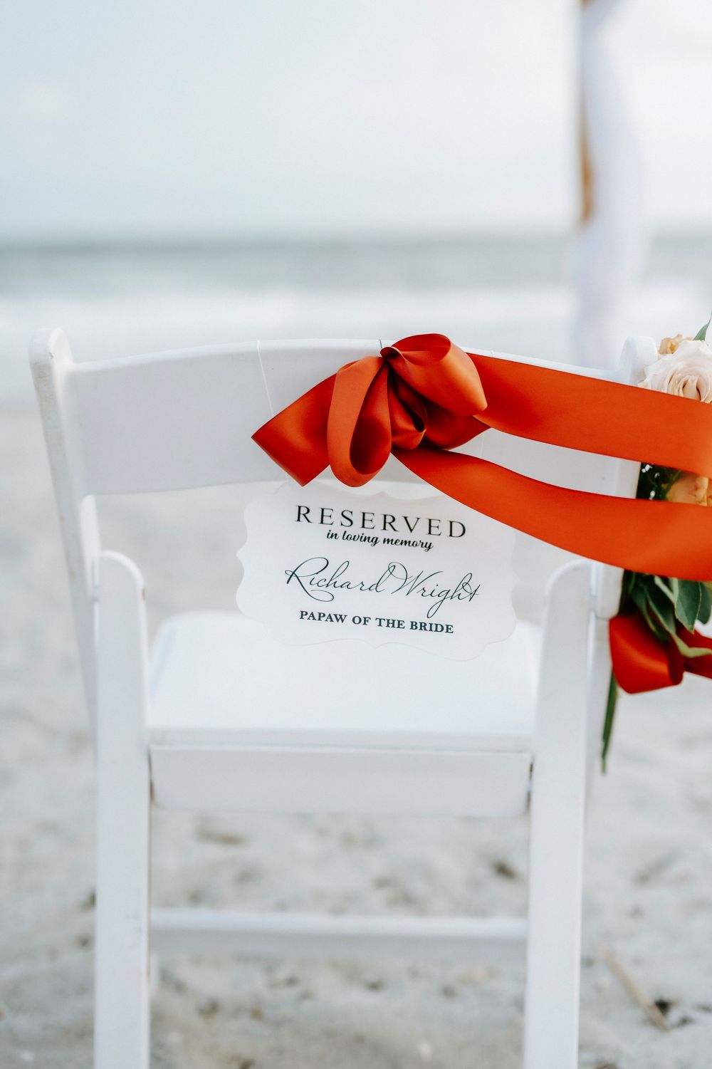 Reserved in loving memory chair sign for Richard Wright, Papaw of the Bride, tied with red ribbon at beach wedding.