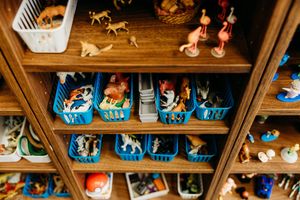 Wooden shelves displaying colorful blue baskets filled with assorted miniature animal figurines and toys neatly organized.