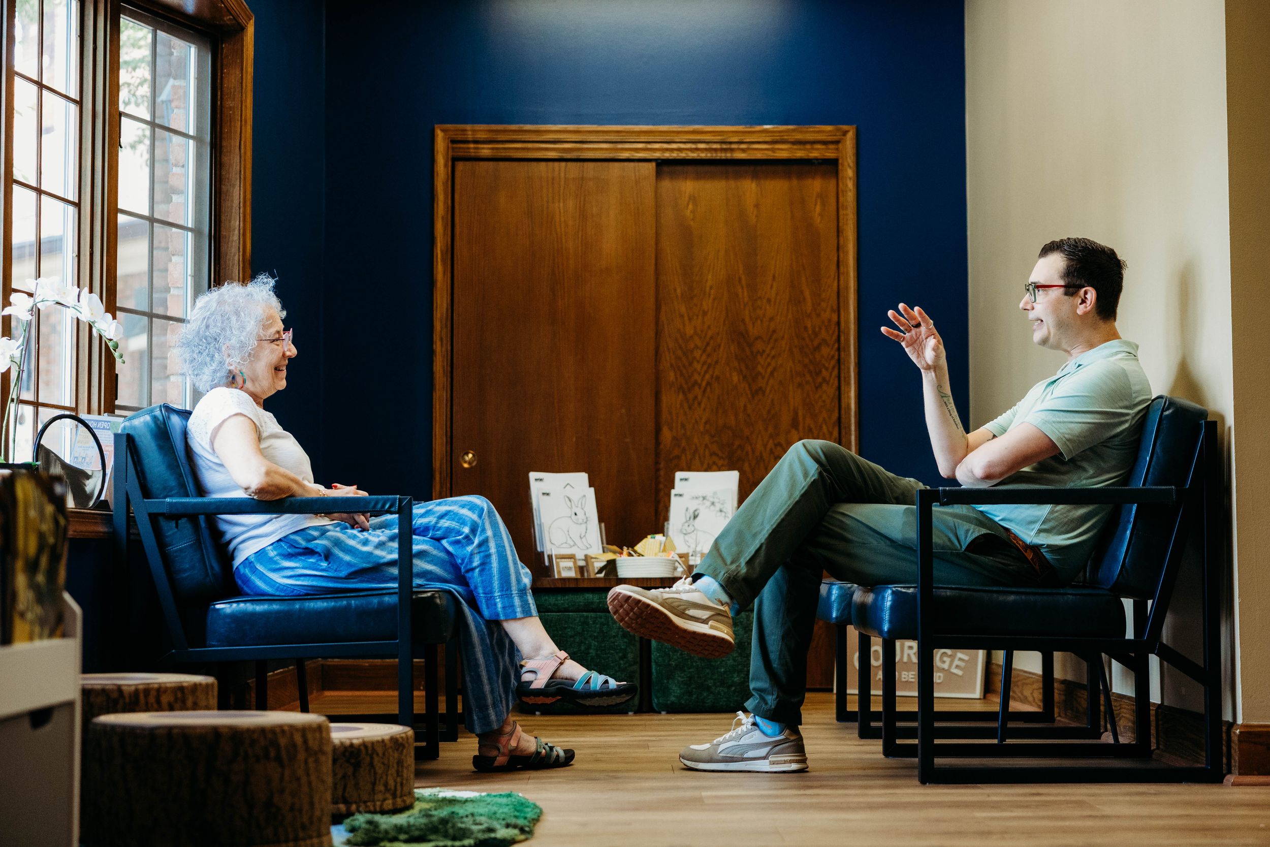 Two people having a conversation in a modern blue office with wooden accents, seated in chairs facing each other.