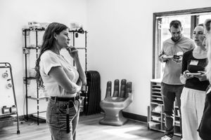 Black and white photo of a woman speaking to a group in a modern studio space with unique hand-shaped chair decor.