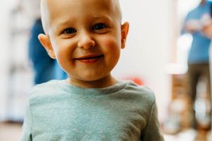Smiling toddler boy with blue eyes wearing a gray t-shirt, looking happy and cheerful indoors.