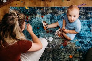 Overhead view of a mother and baby playing together on a colorful blue rug with toys on a hardwood floor.