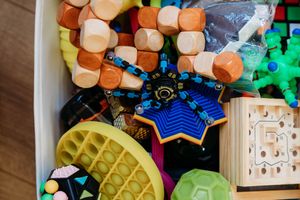 Colorful assortment of children's toys including wooden blocks, pop-it fidget, and building sets in a storage bin.