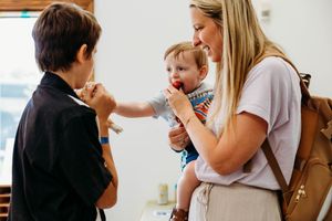 Woman holding a baby while an older child interacts with them indoors.