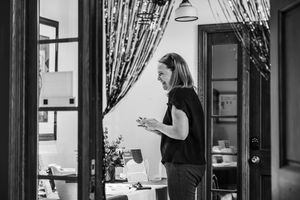 Black and white photo of a woman standing in a doorway holding a cup in a stylish interior space.