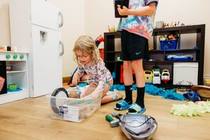 Two children playing in a colorful playroom, one sorting items in a plastic bin on the floor.