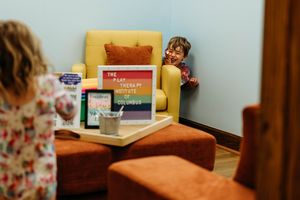 Children play in a cozy therapy office with yellow chairs and a colorful Play Therapy Institute Columbus sign.