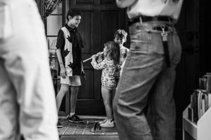 Black and white photo of children playing near a doorway while adults stand in the foreground.