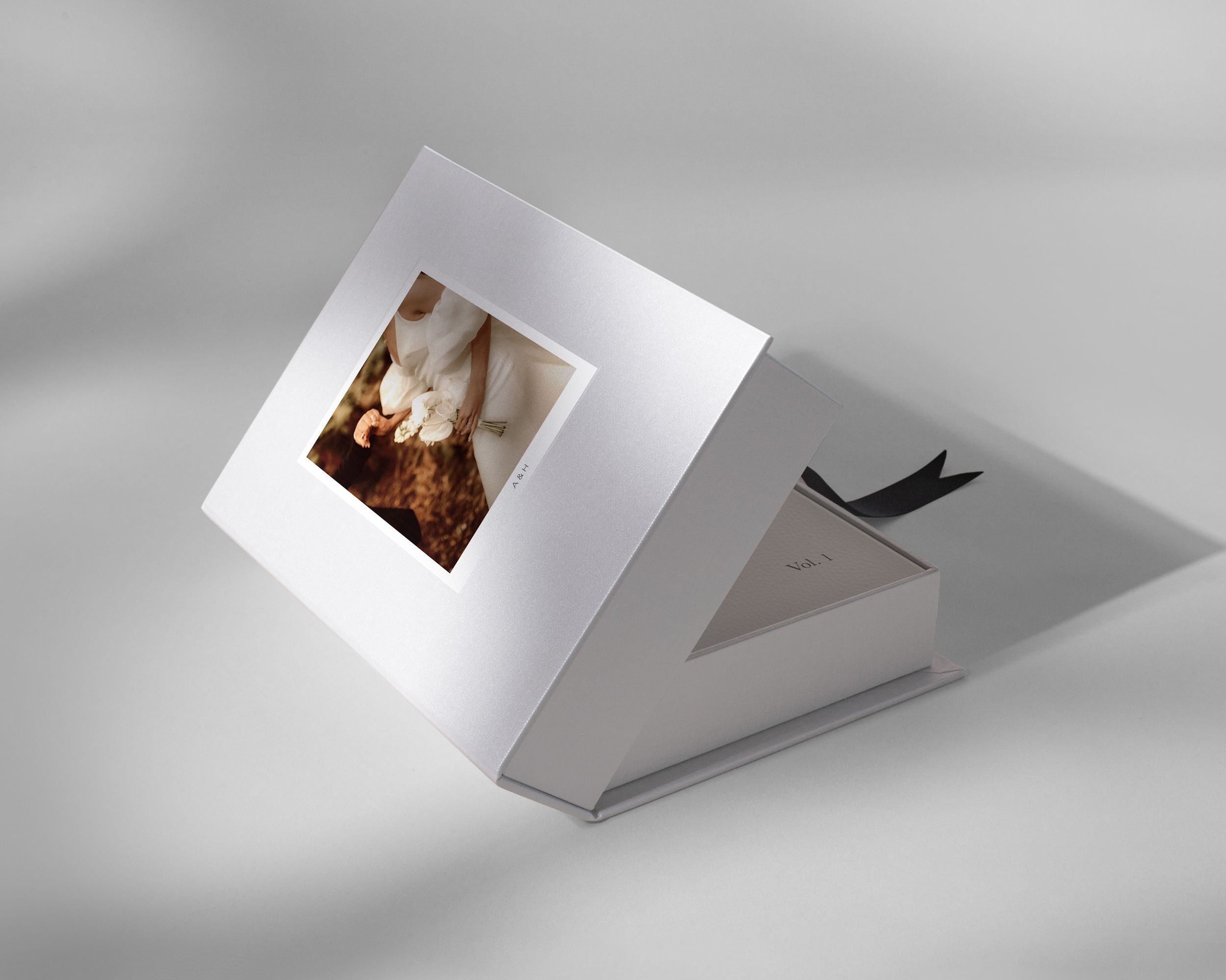 White luxury photo box with square window displaying a fine art print, tilted at an angle on a neutral background.