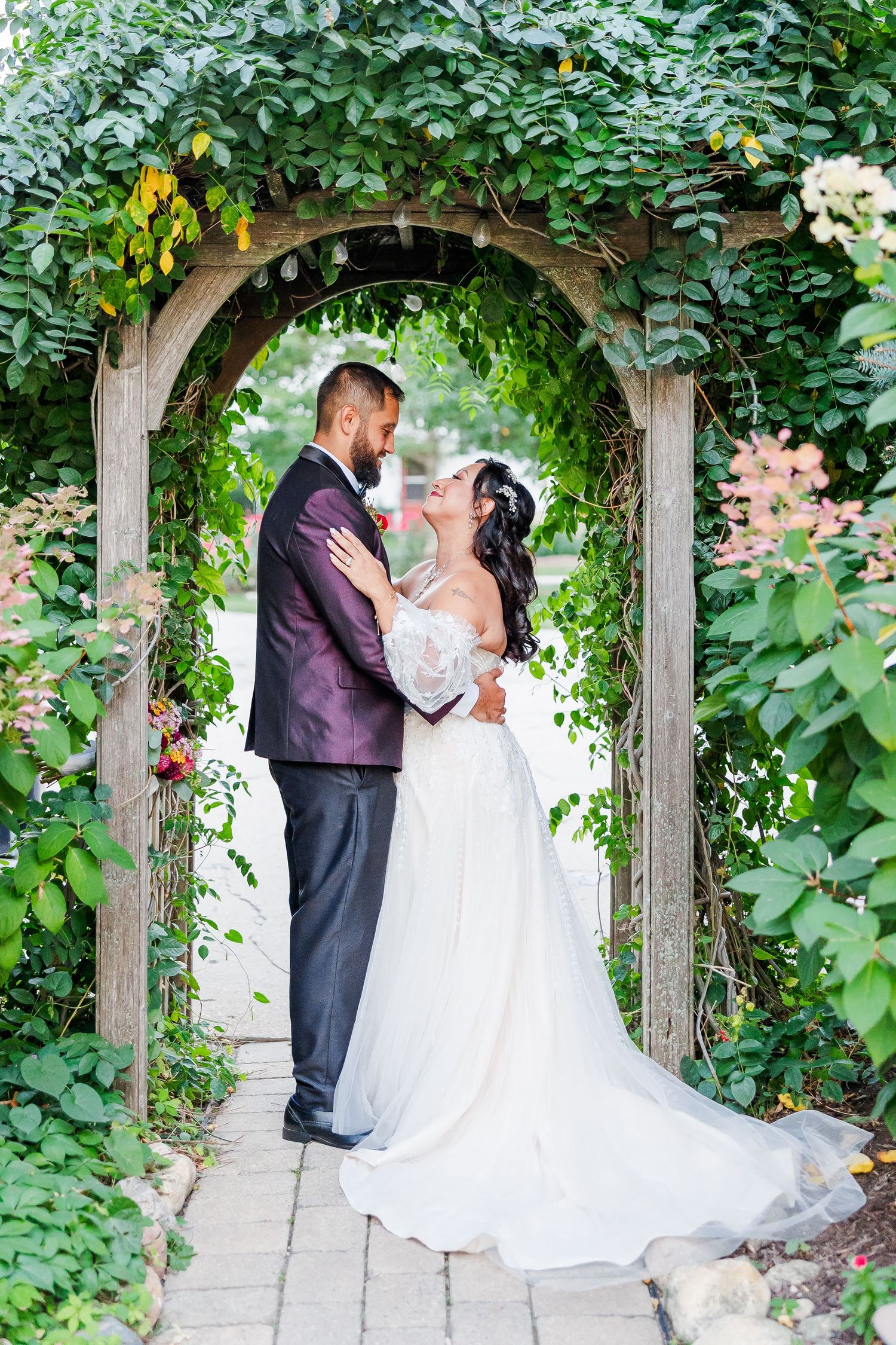 Bride and groom share a romantic kiss under a lush green garden archway on their wedding day.