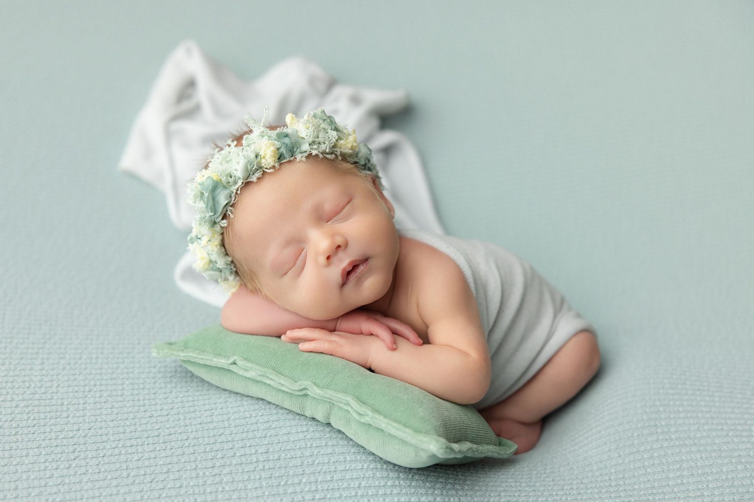 Peaceful newborn baby swaddled in cream wrap sleeping on soft beige blanket during professional newborn photography session.