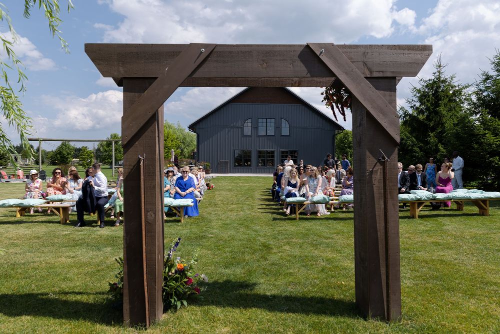 Outdoor wedding reception on green lawn with wooden arbor and guests seated on benches at barn swallow fields in guelph, ontario.