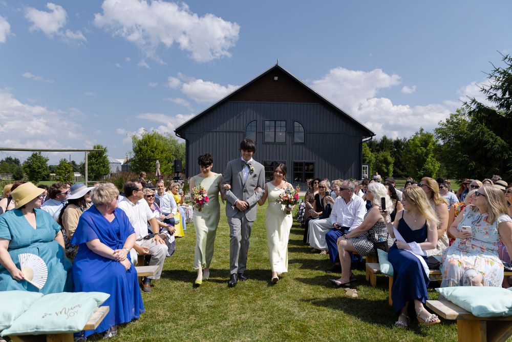 Outdoor wedding ceremony with wedding party walking down aisle and guests seated on benches at barn swallow fields in guelph, ontario.