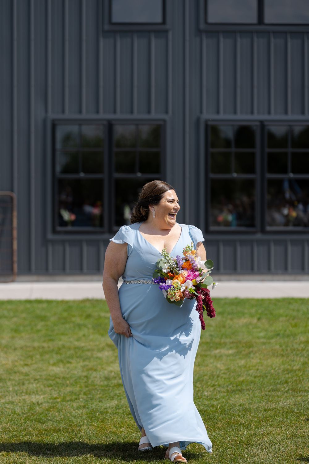 Smiling bridesmaid in light blue gown walks down aisle of outdoor wedding ceremony at barn swallow fields in guelph, ontario.