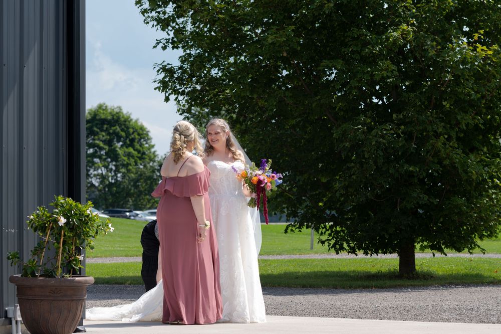 Bride in white gown and bridesmaid in pink dress standing outdoors near a barn at barn swallow fields in guelph, ontario.