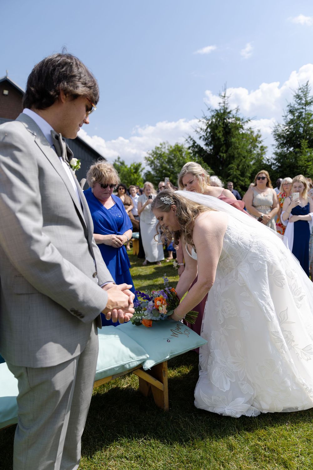 Bride at outdoor wedding ceremony, setting colorful bouquet on a pillow during the ceremony at barn swallow fields in guelph, ontario.