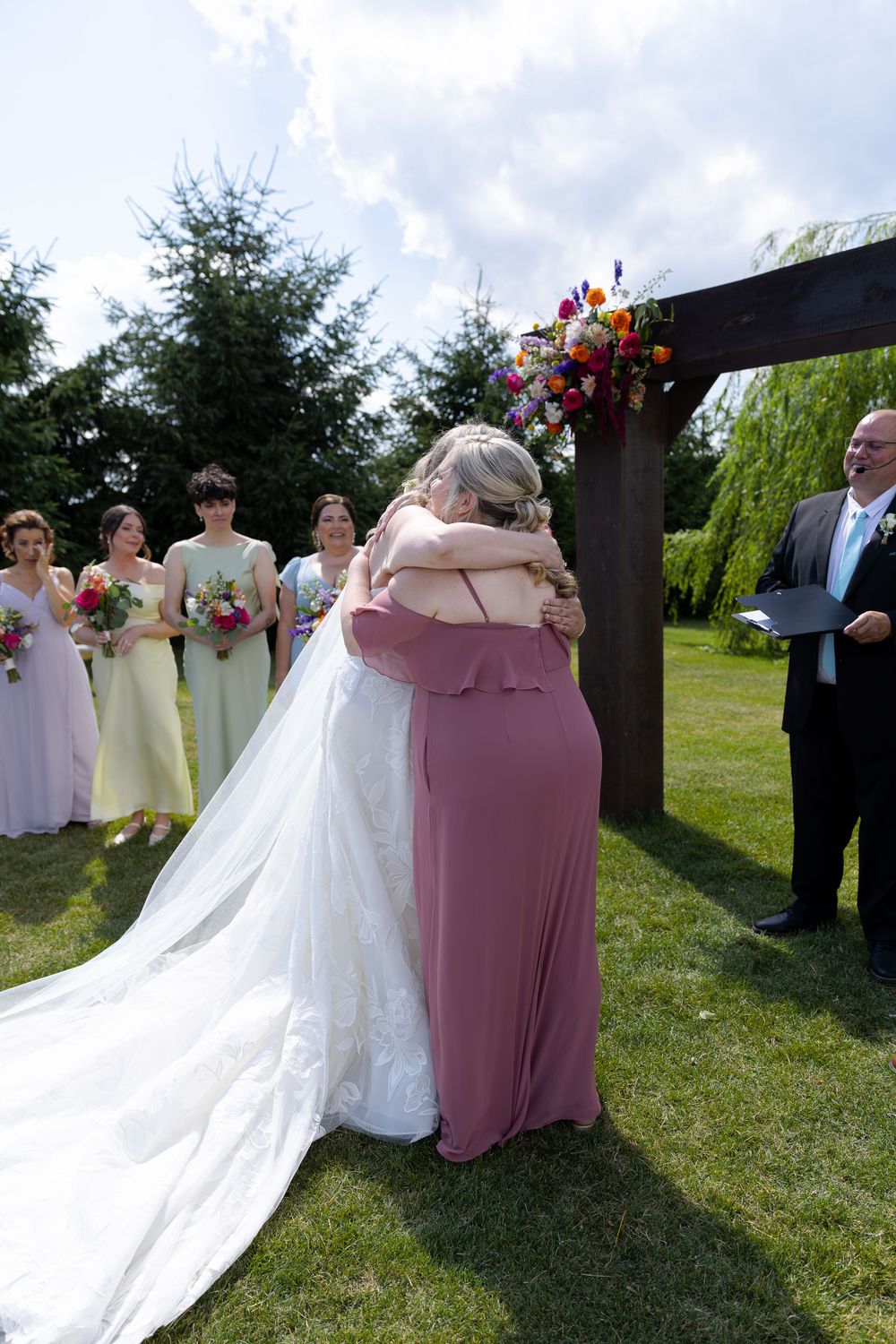 Bride and bridesmaid hug at outdoor wedding ceremony at barn swallow fields in guelph, ontario.