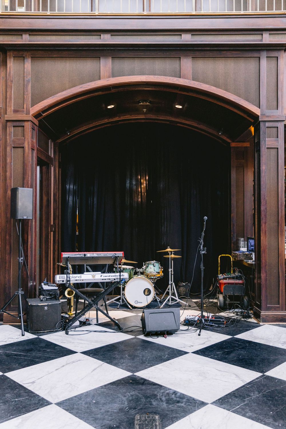 Band instruments set up on black and white checkered floor in front of elegant wooden arched stage.