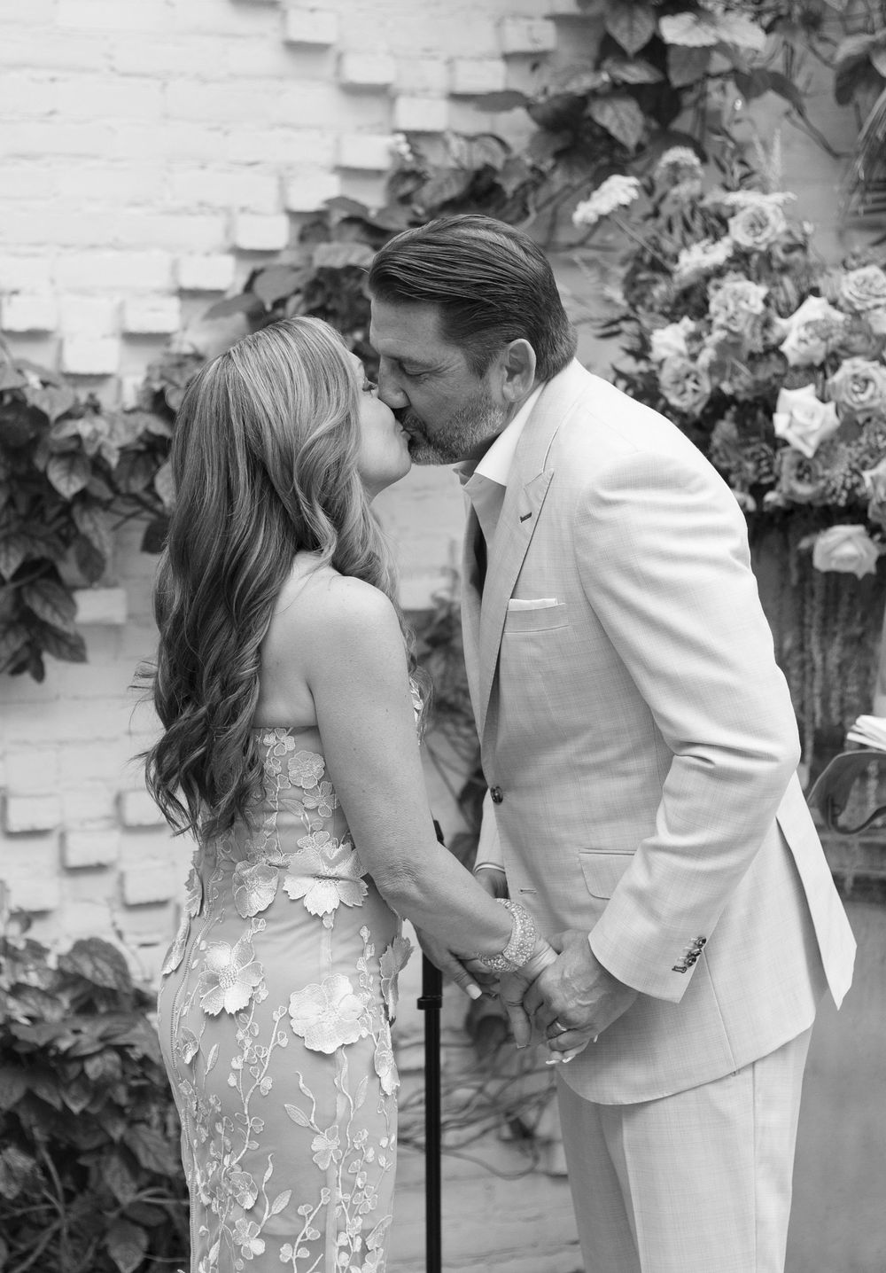 Black and white photo of a couple sharing a first kiss at their wedding ceremony outdoors.