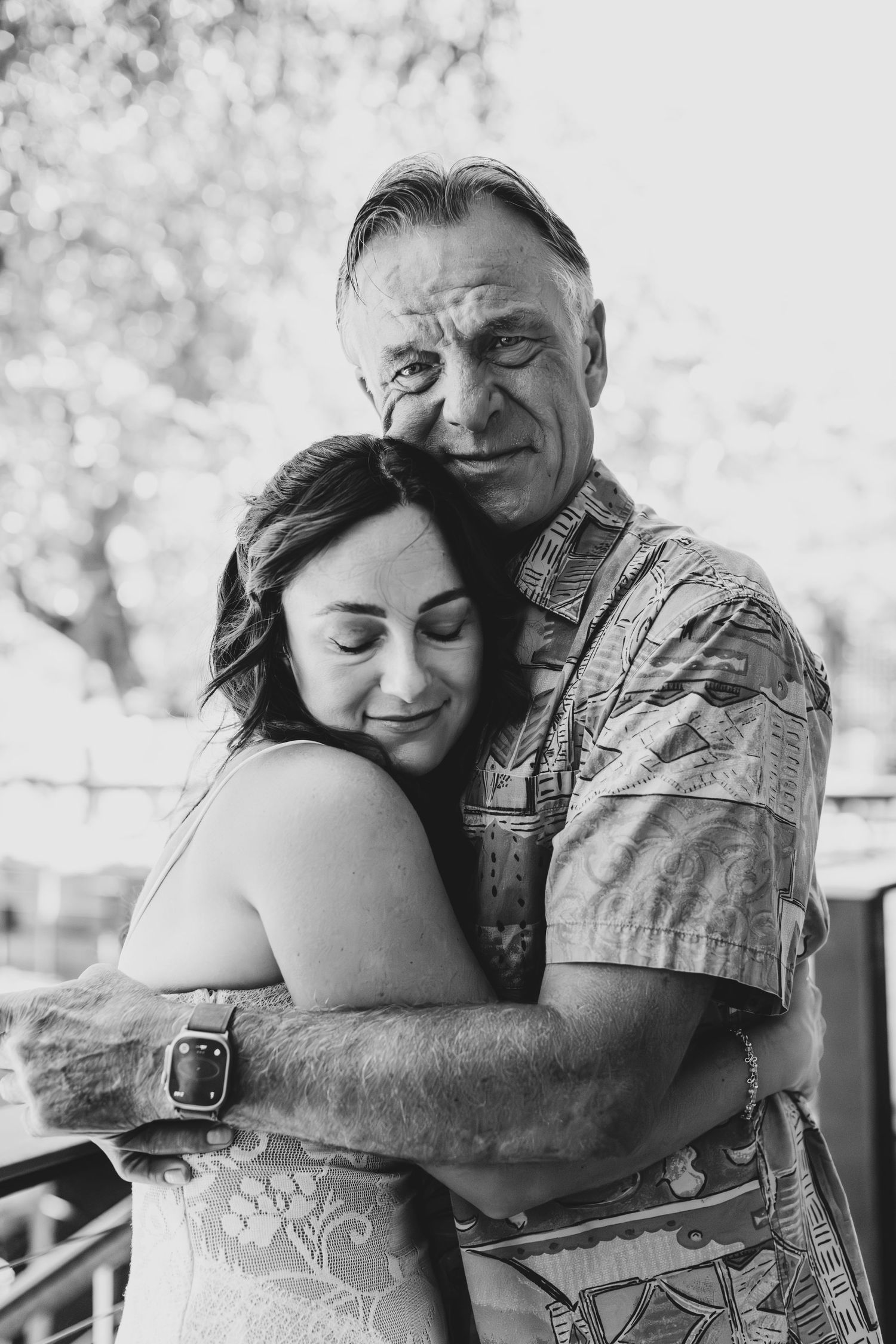 Black and white photo of an older man and young woman sharing a warm embrace outdoors.