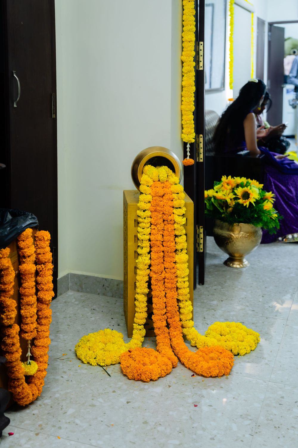 Vibrant orange and yellow marigold flower garlands spilling from brass pot at Indian wedding entrance.