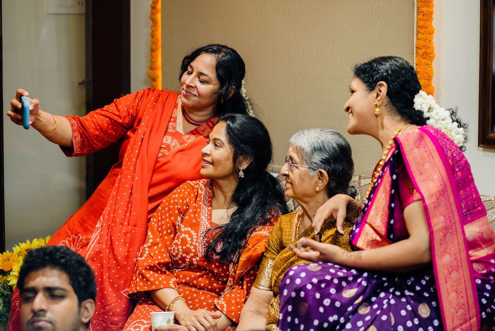 Four Indian women in colorful sarees taking a selfie together during a festive celebration.