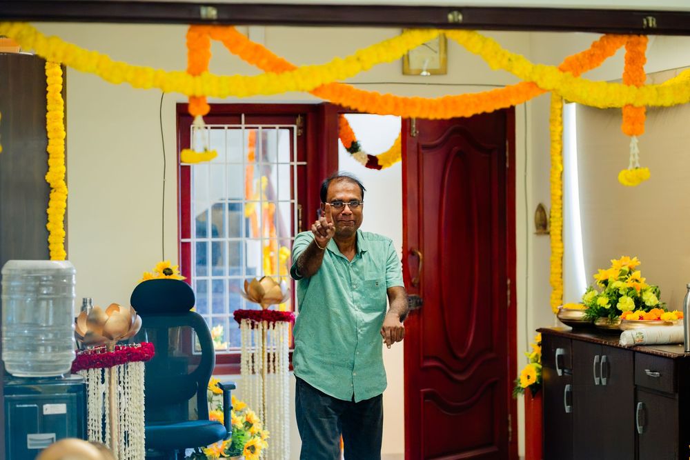 Indian man speaking at microphone in home decorated with marigold garlands during traditional celebration.