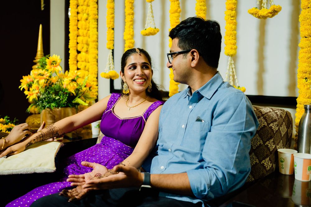 Indian couple in traditional attire sitting together, smiling, surrounded by yellow marigold flower decorations.