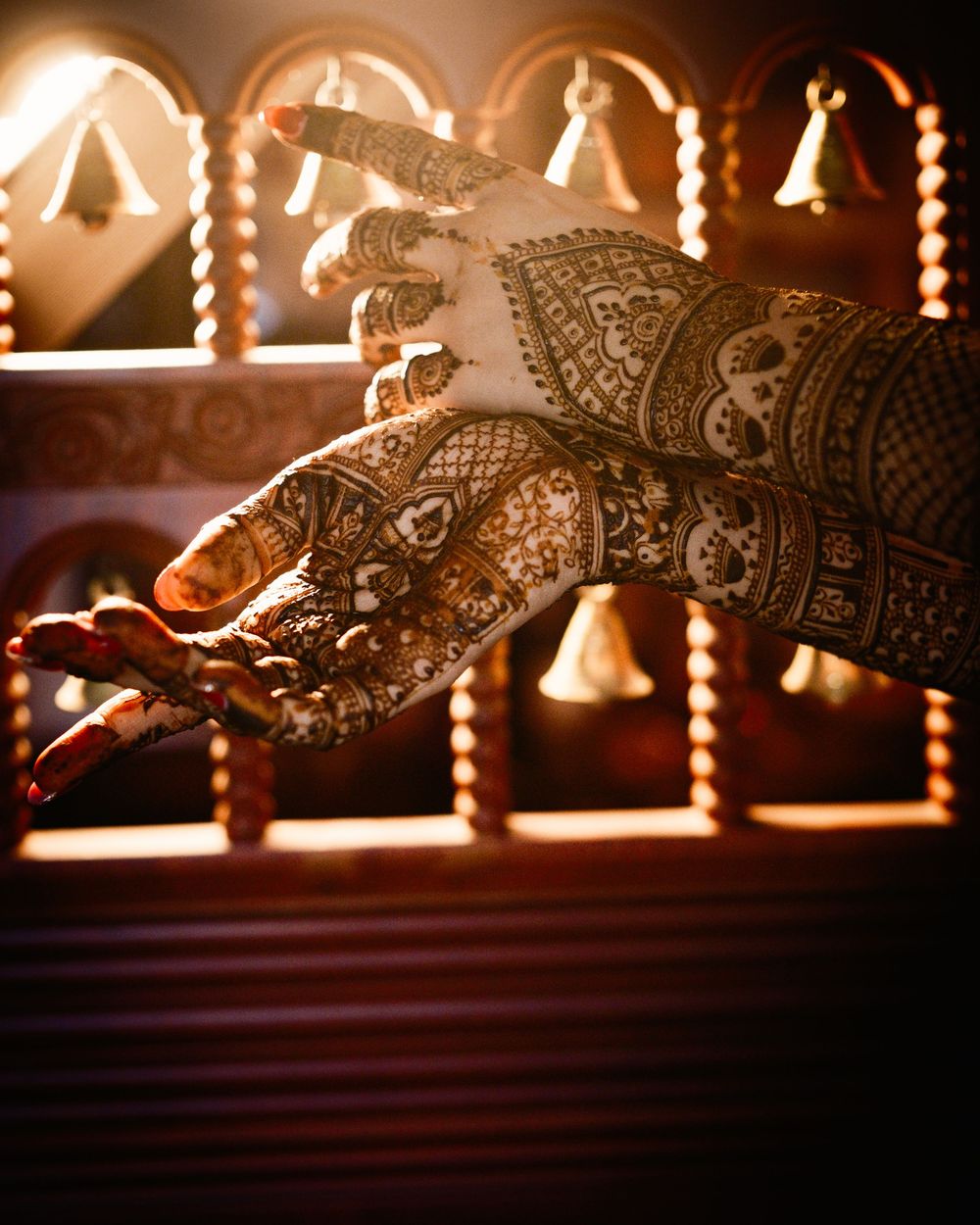 A hand adorned with intricate dark henna mehndi design, photographed against a warmly lit decorative backdrop.