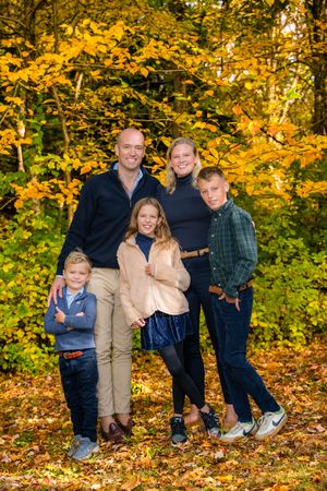 Family of five posing together in autumn forest with golden yellow foliage, wearing coordinated fall outfits.
