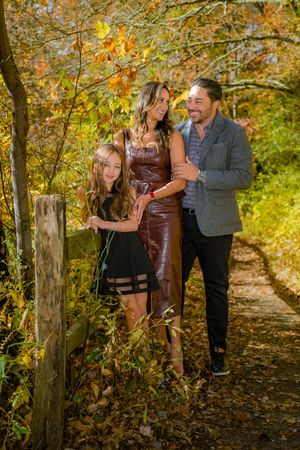 Family of three posing on an autumn forest path surrounded by colorful fall foliage.