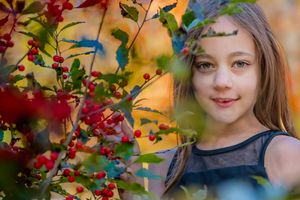 Young girl smiling among vibrant autumn foliage with red berries in a colorful fall outdoor portrait.