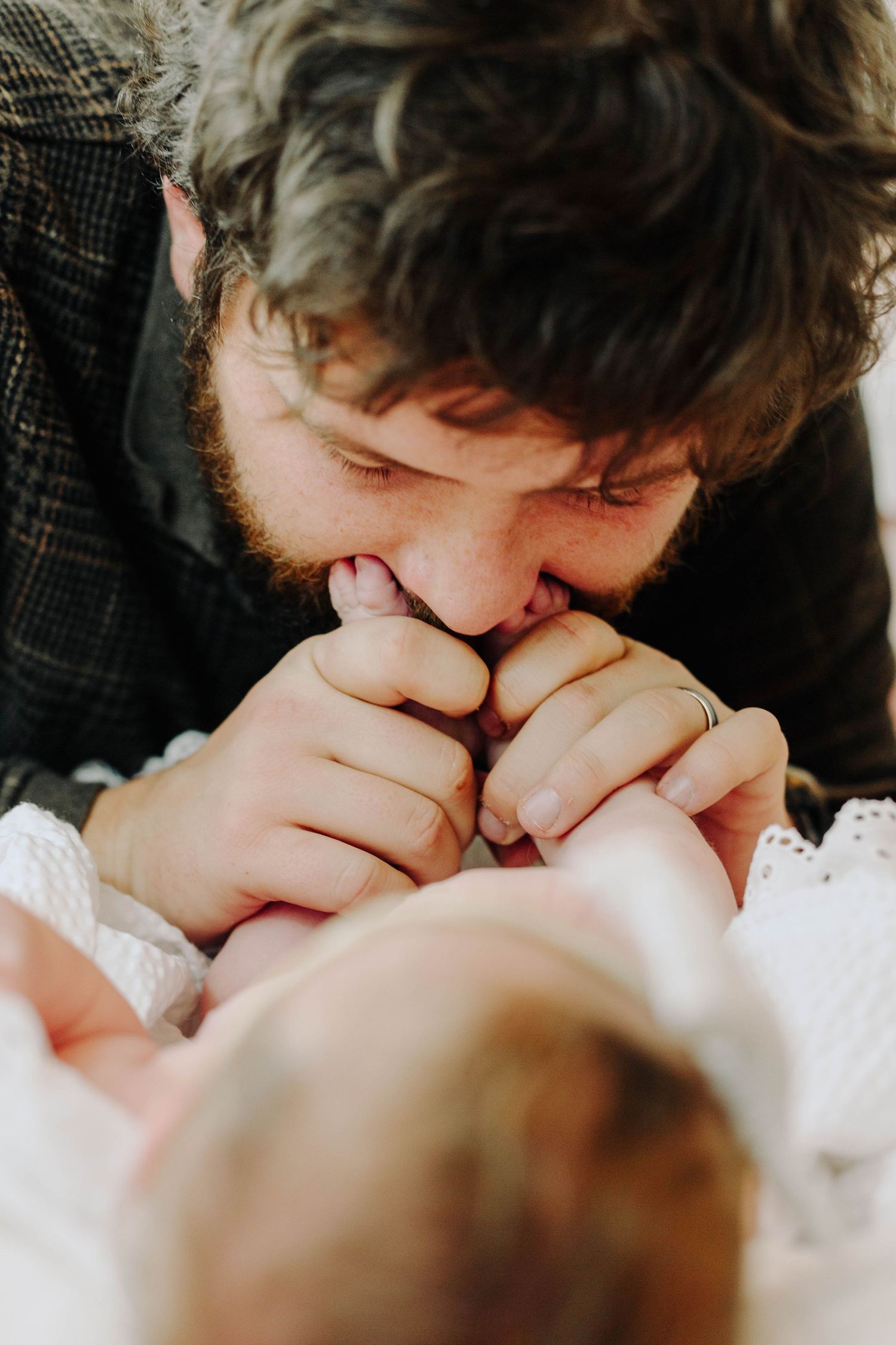 A bearded father tenderly kisses his newborn baby's tiny hands while wearing a wedding ring.
