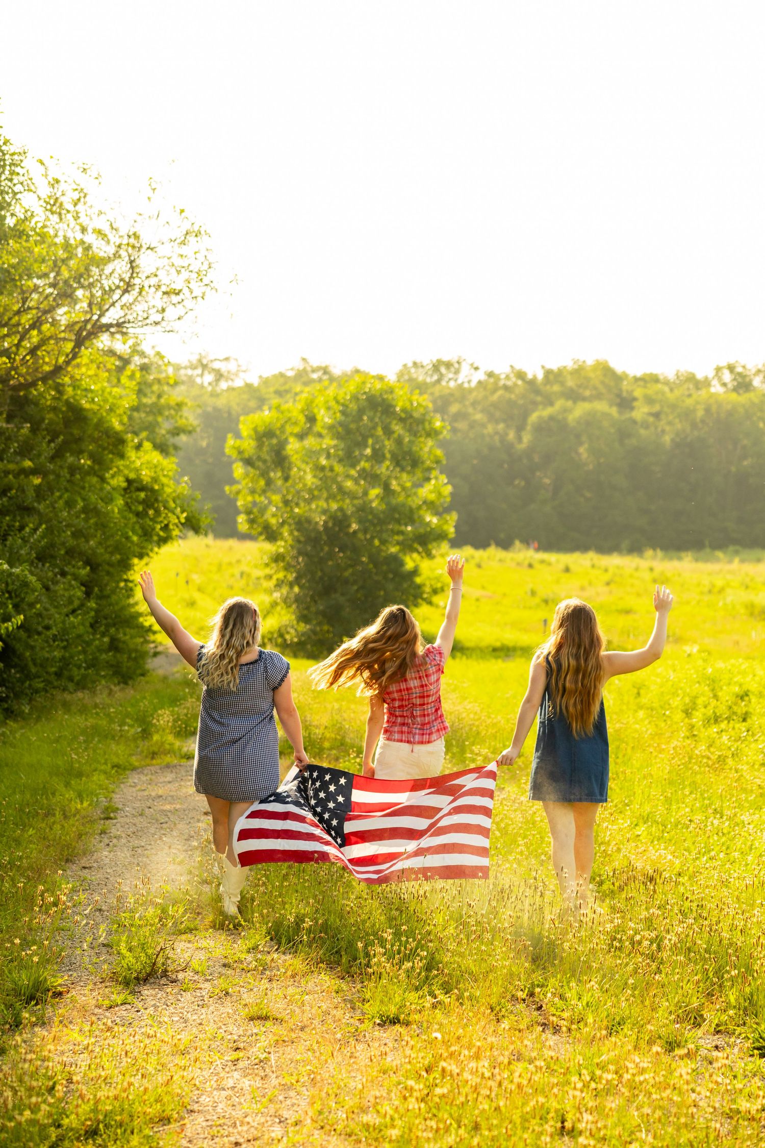 A group of young women in colorful summer outfits dancing and playing on a green lawn near a wooden fence.